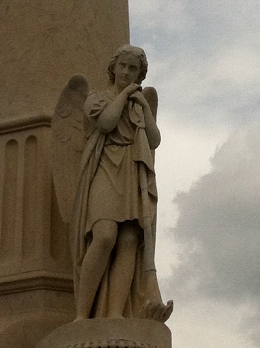 An angel leans against his trumpet at the base of the monument. 