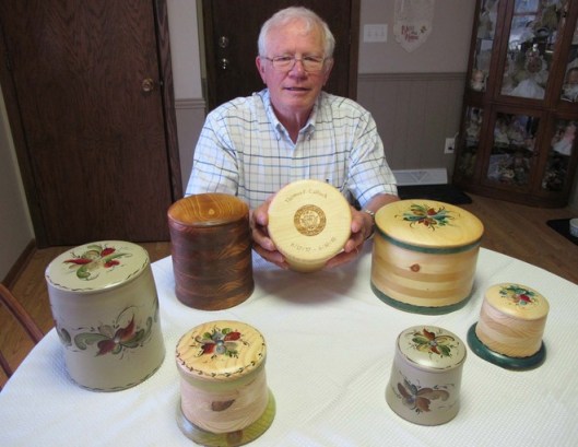 Tom Caflisch of River Falls, Wisc. holds a wooden urn his remains will be placed in someday. A Navy veteran, he etched the dates of his military service on the lid. In his part-time urn business, he personalizes cremation urns for customers who want their military service or other identification noted on their burial urns. Photo courtesy of Meg Jones/Milwaukee Journal Sentinel.